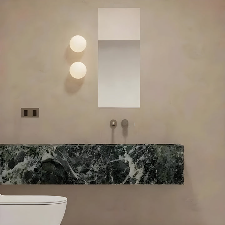 Minimalist wall sconce with spherical frosted glass shade installed beside a modern bathroom vanity mirror