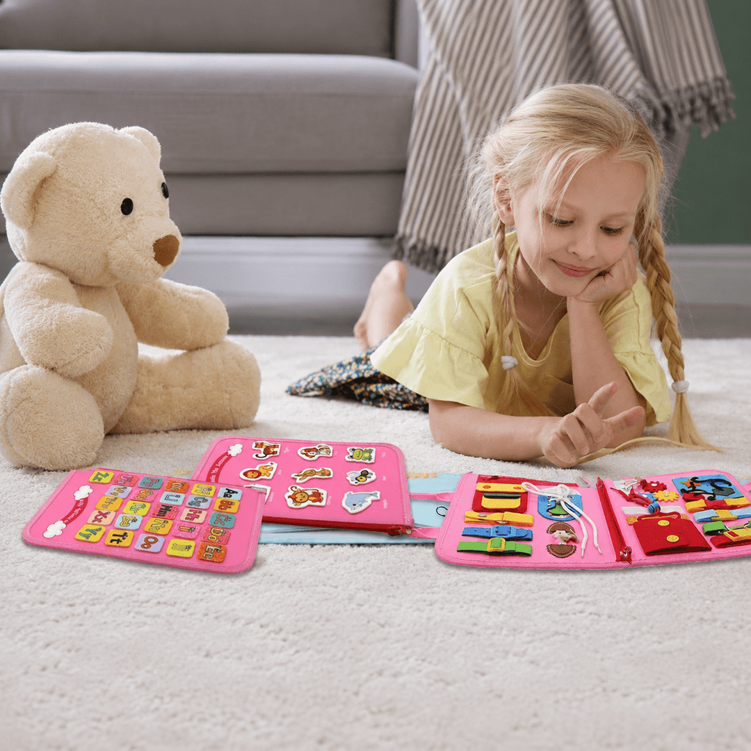 Young girl playing happily with a pink Montessori busy board toy on the floor