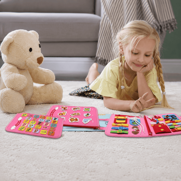 Young girl playing happily with a pink Montessori busy board toy on the floor
