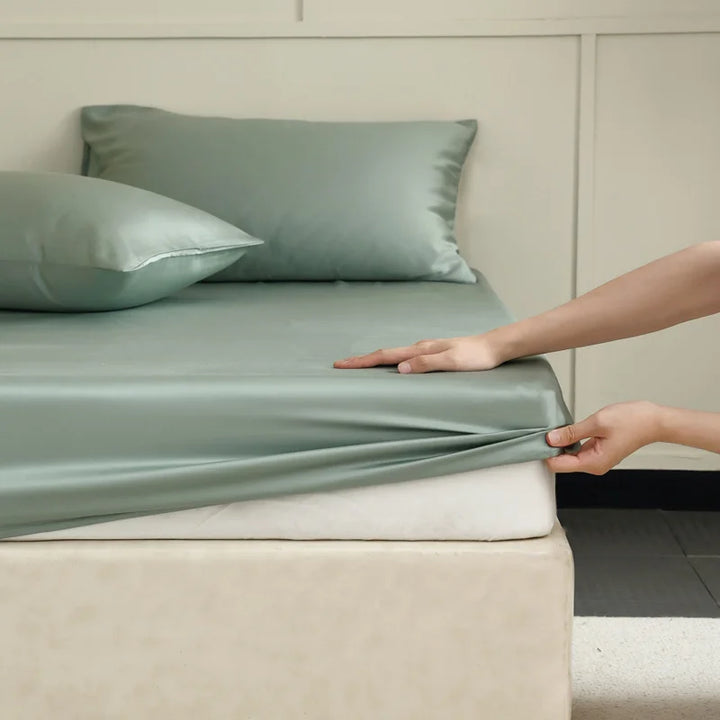 Hands smoothing an emerald green silk bed sheet over a made mattress