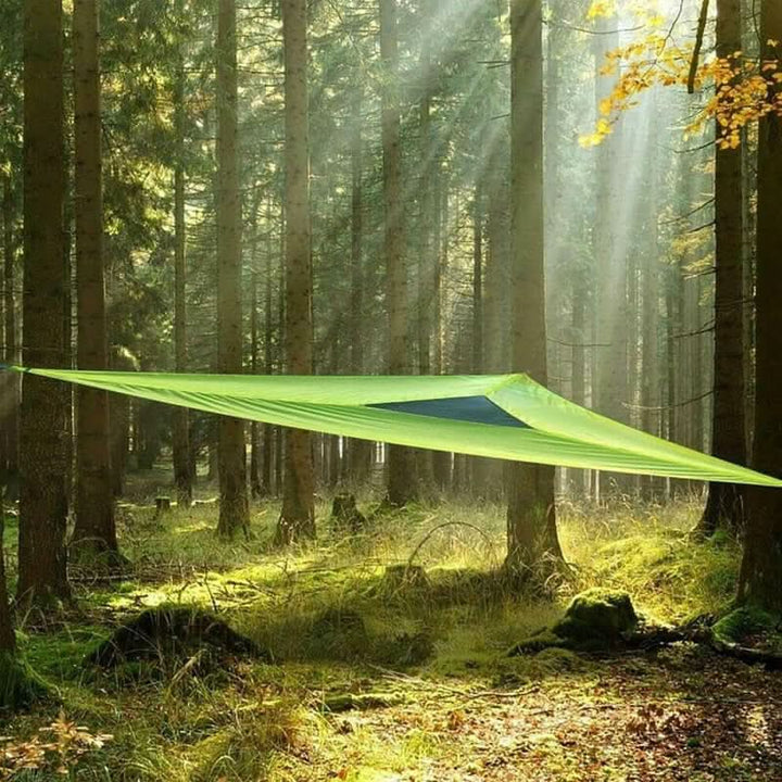 Green triangular camping hammock hung between trees in a forest