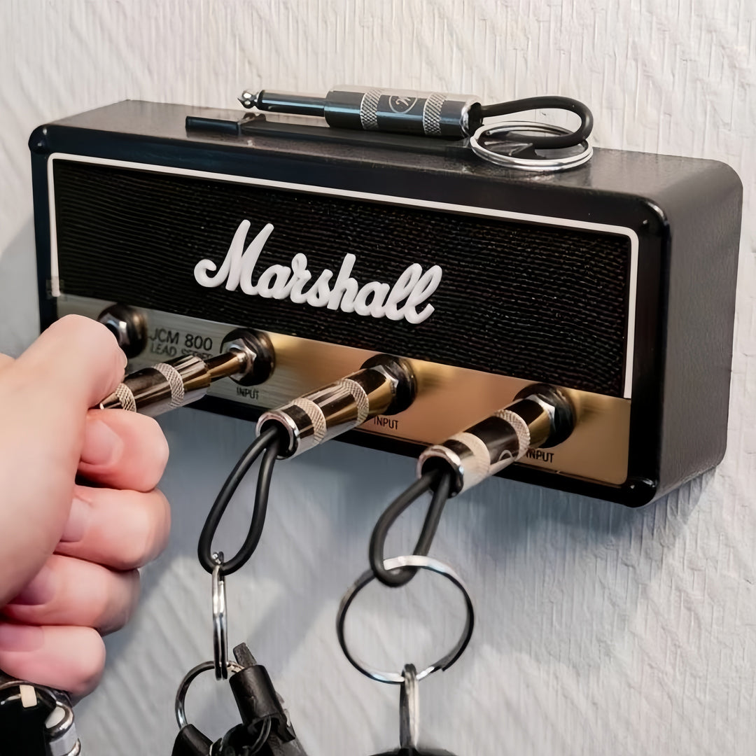 Black amplifier key holder mounted on a wall with a guitar plug keychain plugged in