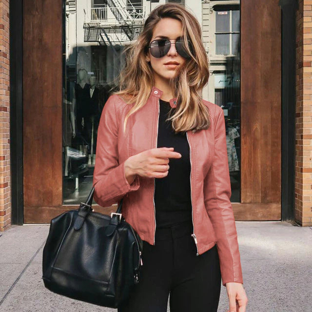 Woman wearing pink zip-up jacket posing with a black handbag in front of a storefront