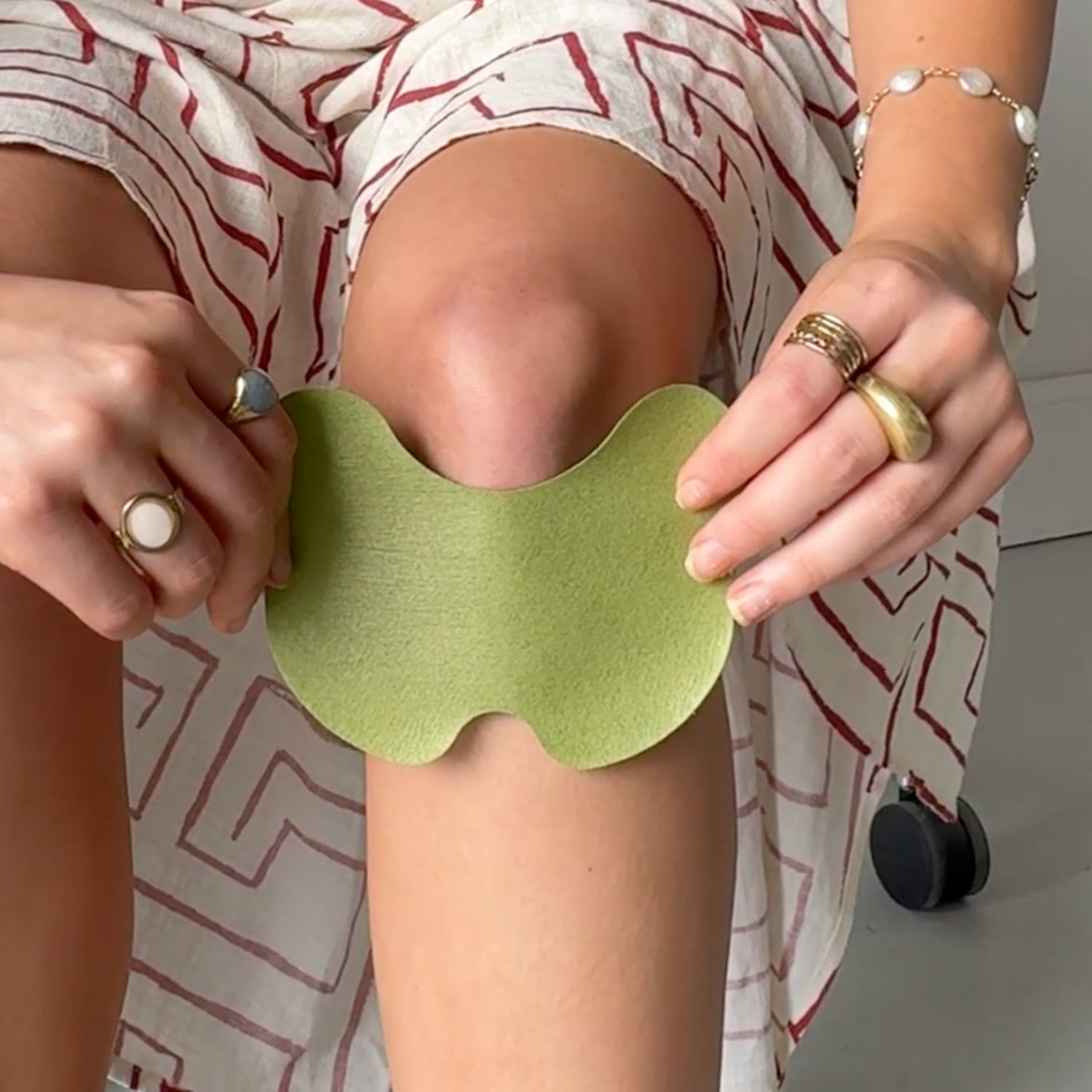 Person holding a green herbal knee pain relief patch against their leg