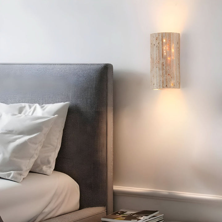 Natural stone LED wall sconce light casting warm illumination beside a modern upholstered bed