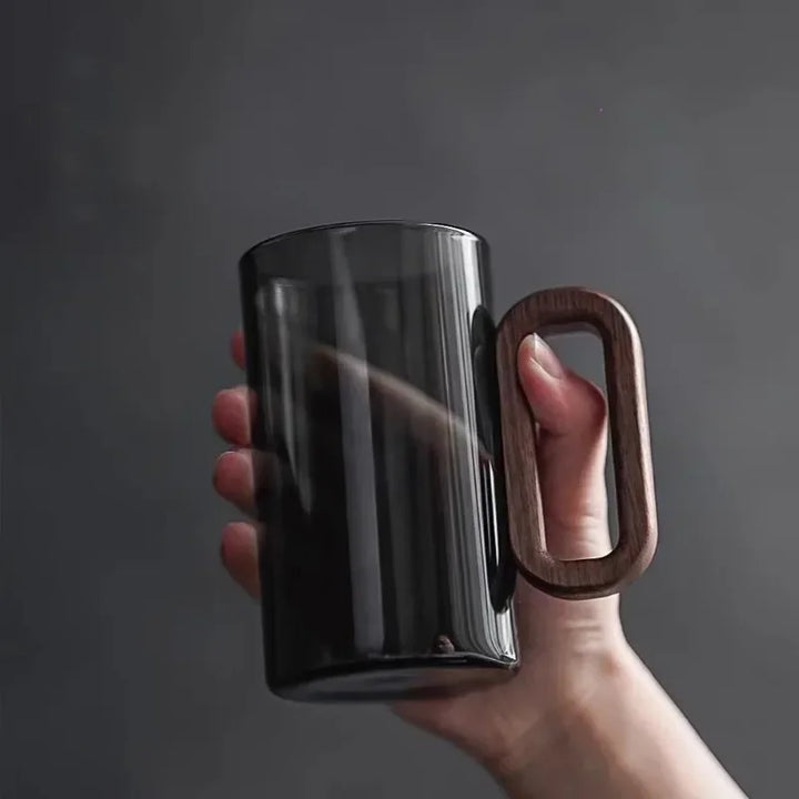 Smoky gray glass mug held in a hand showing the wooden handle