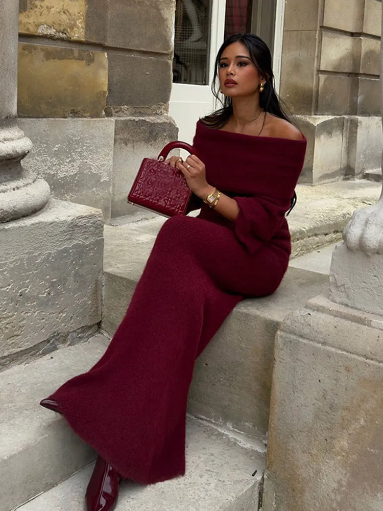 Woman sitting on stone steps wearing a red off-shoulder knitted maxi dress holding a matching bag