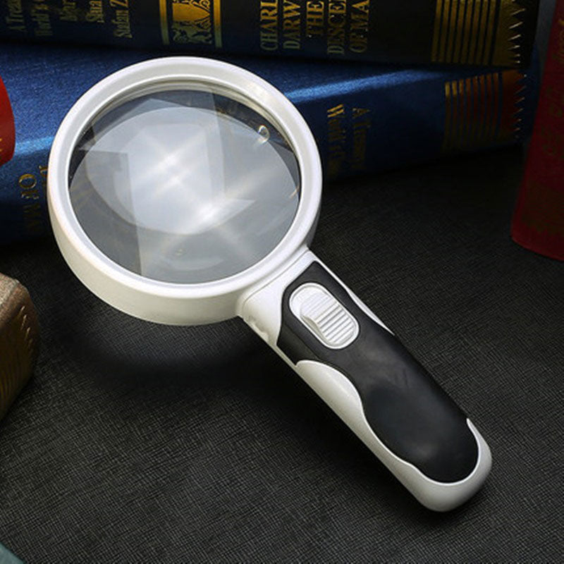 Optical magnifying glass resting on a dark surface next to books