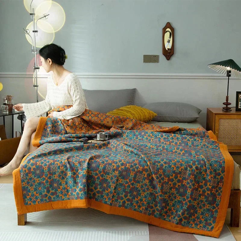 Woman sitting on a bed draped with an orange and blue patterned six-layer quilt