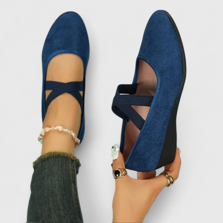 Blue orthopedic wedge sandal held in hand showing crisscross strap design