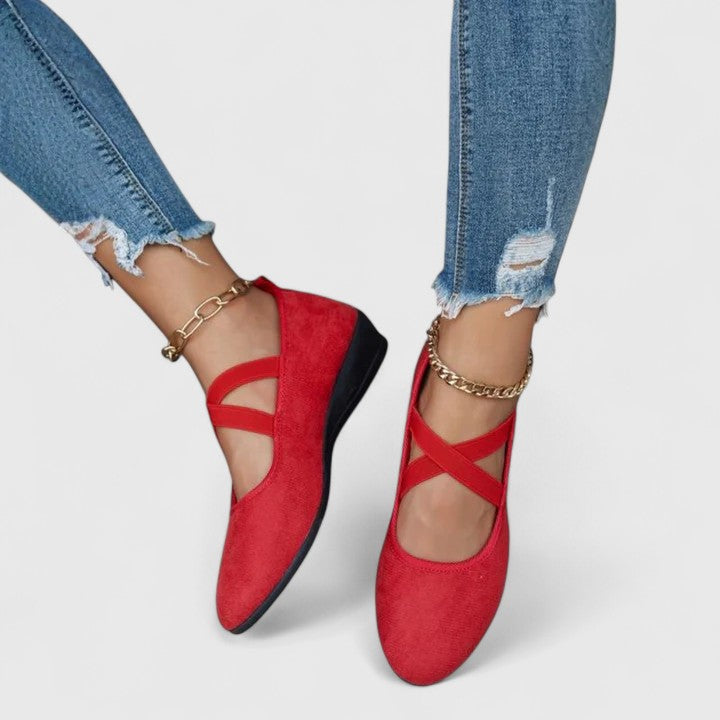 Red orthopedic wedge sandals worn on feet with distressed blue jeans