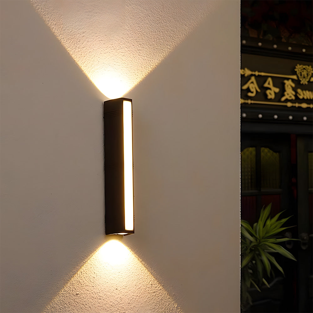 Minimalist black LED outdoor wall light casting warm upward and downward beams on an exterior wall.