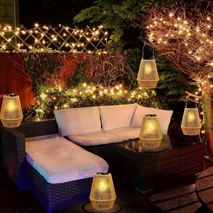 Multiple solar lanterns hanging and placed on patio furniture in a garden at night