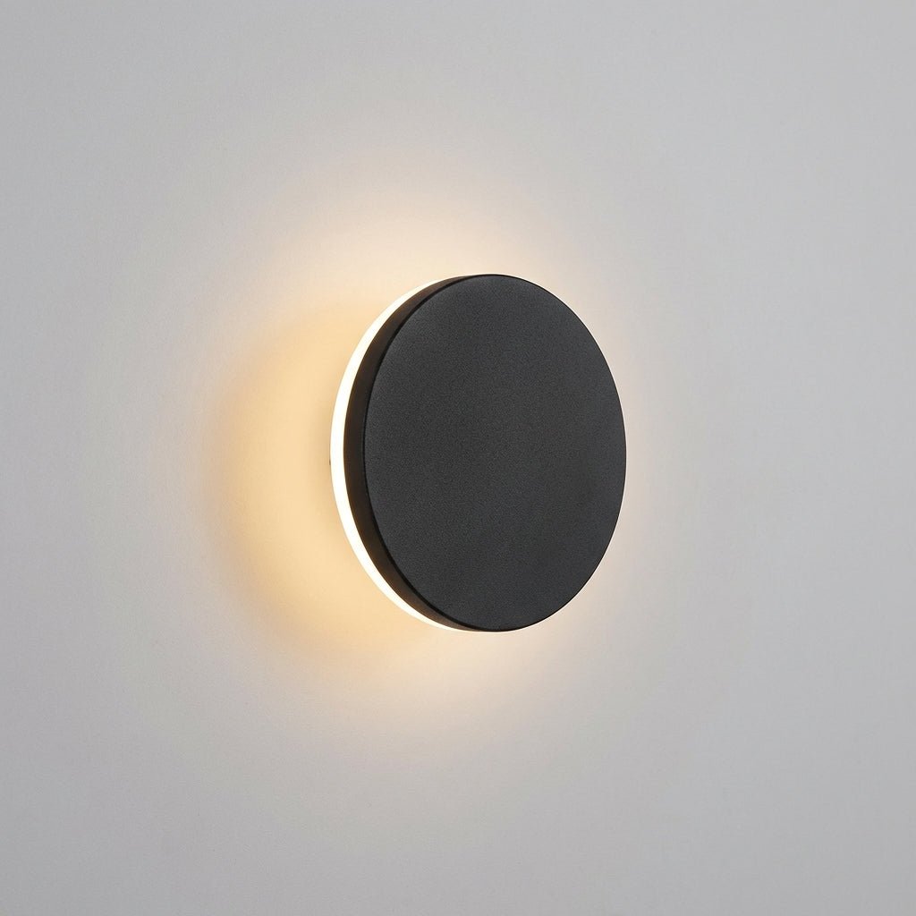 Minimalist black round wall light glowing against a neutral wall
