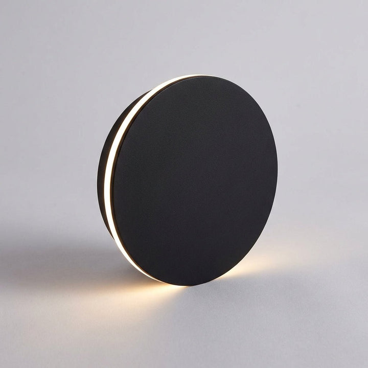 Modern black circular outdoor wall lamp casting up and down light on grey background