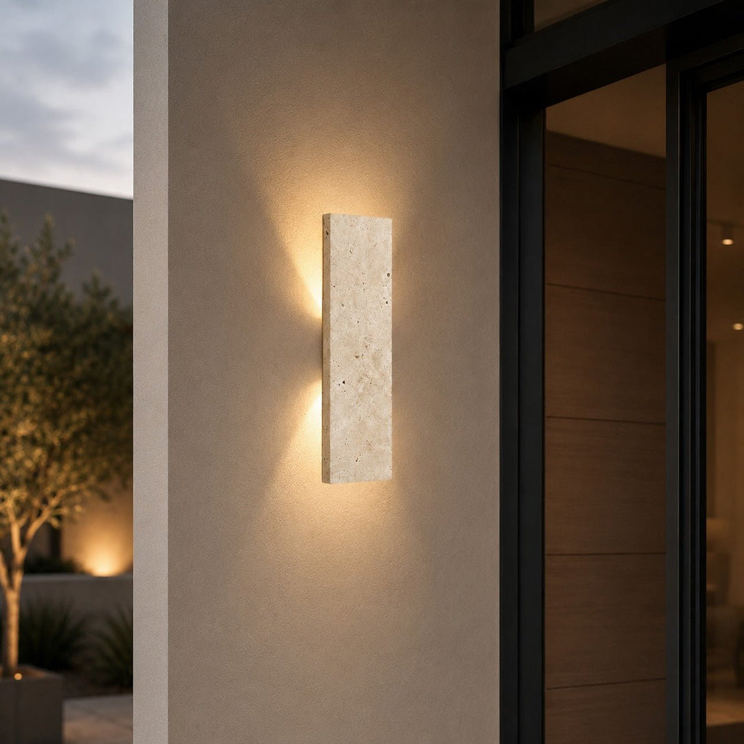 Natural stone outdoor wall light glowing on an exterior wall at dusk
