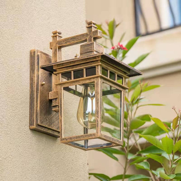 Copper finish outdoor lantern wall light mounted near green foliage