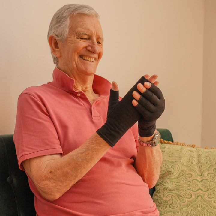 Elderly man smiling while wearing black therapeutic compression gloves