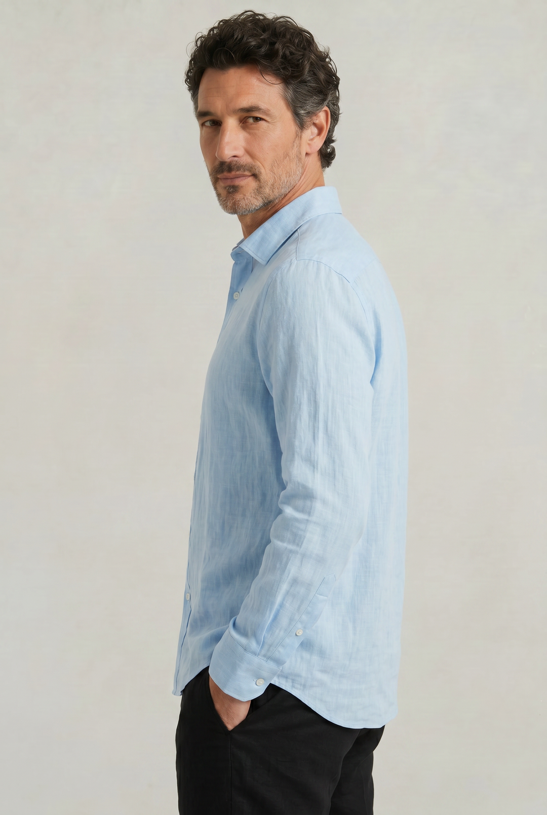 Side profile view of a man wearing a light blue long sleeve button-down shirt
