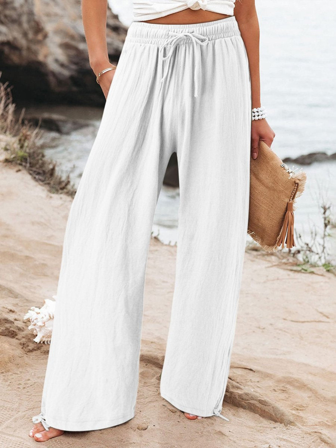 Model wearing white relaxed wide leg pants with a drawstring waist at the beach