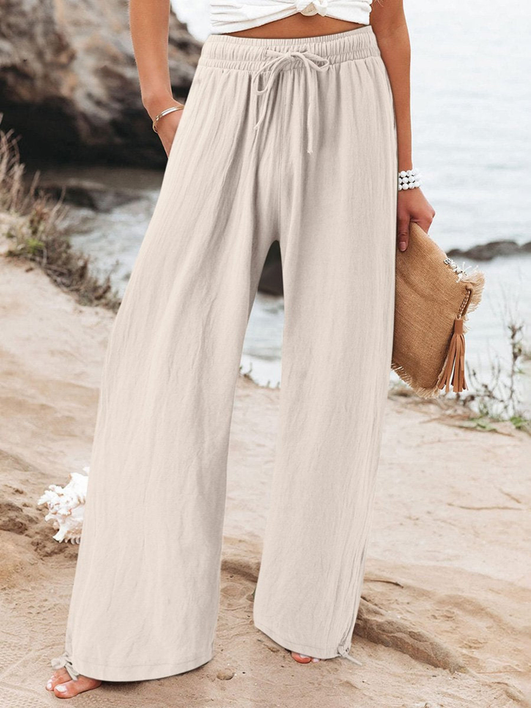 Model wearing almond relaxed wide leg pants with a drawstring waist by the water