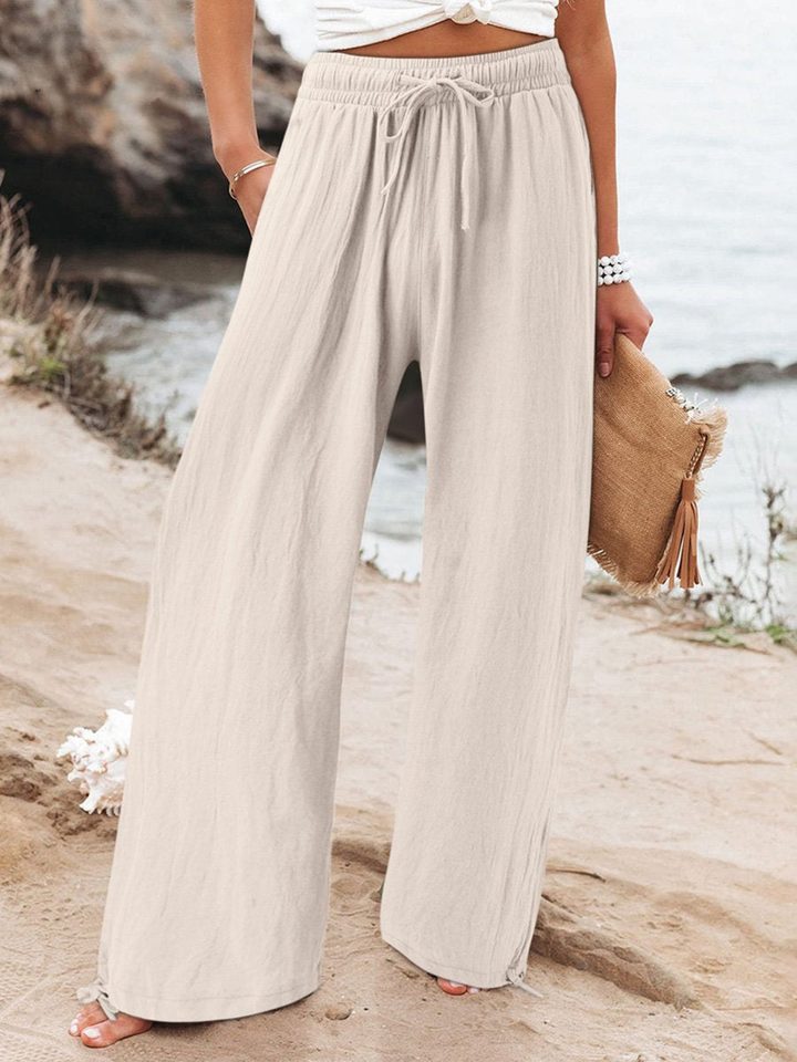 Model wearing almond relaxed wide leg pants with a drawstring waist by the water