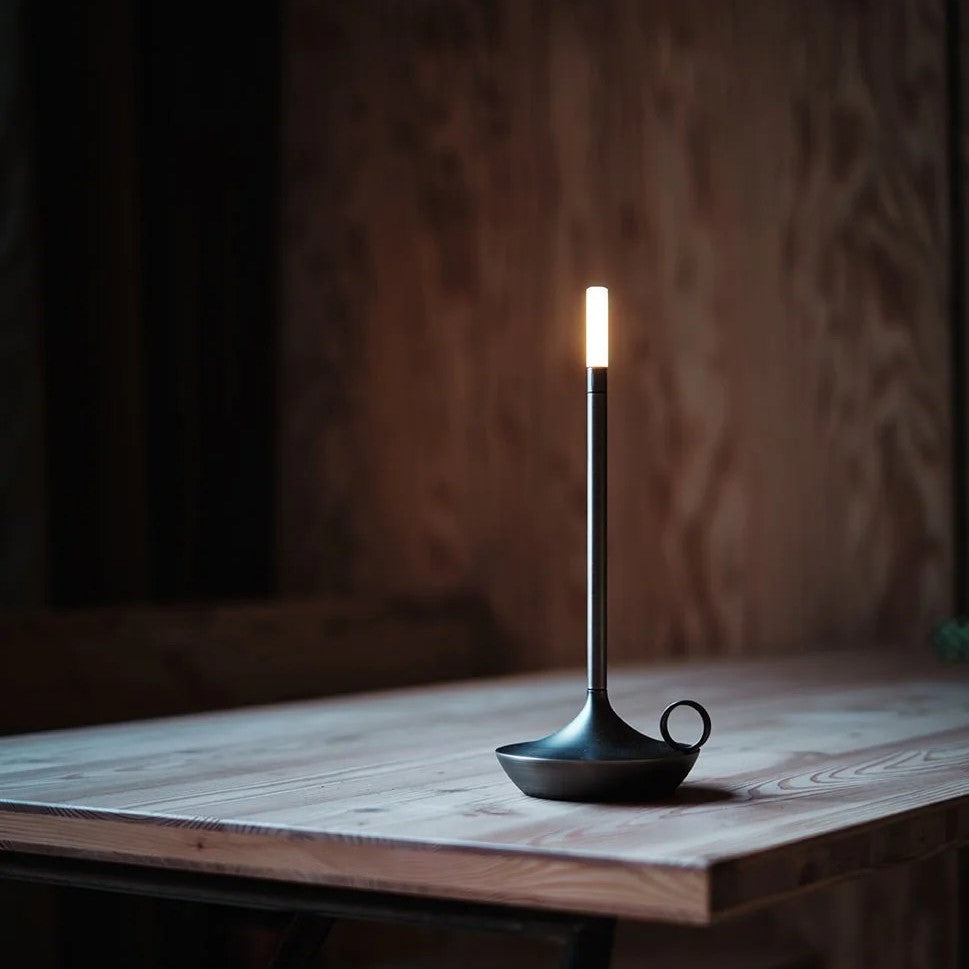 Black cordless LED candle lamp glowing on a wooden table