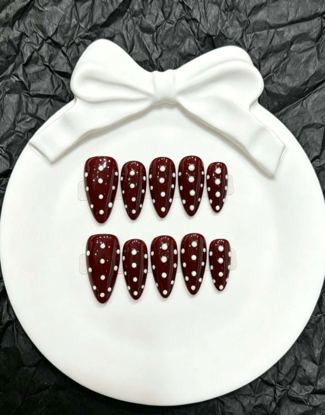 Women's polka dot press-on nail set displayed on a white decorative dish