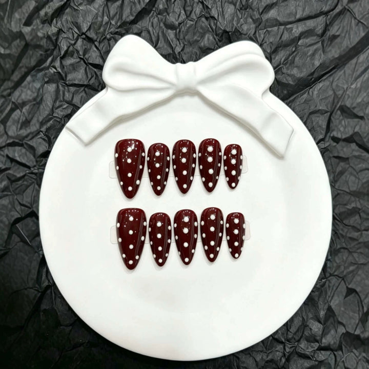 Close-up view of maroon press-on nails with white polka dots