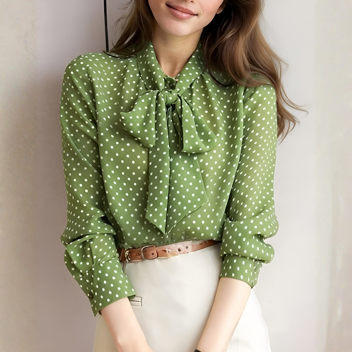 Model wearing a green polka dot tie-neck blouse with a light skirt