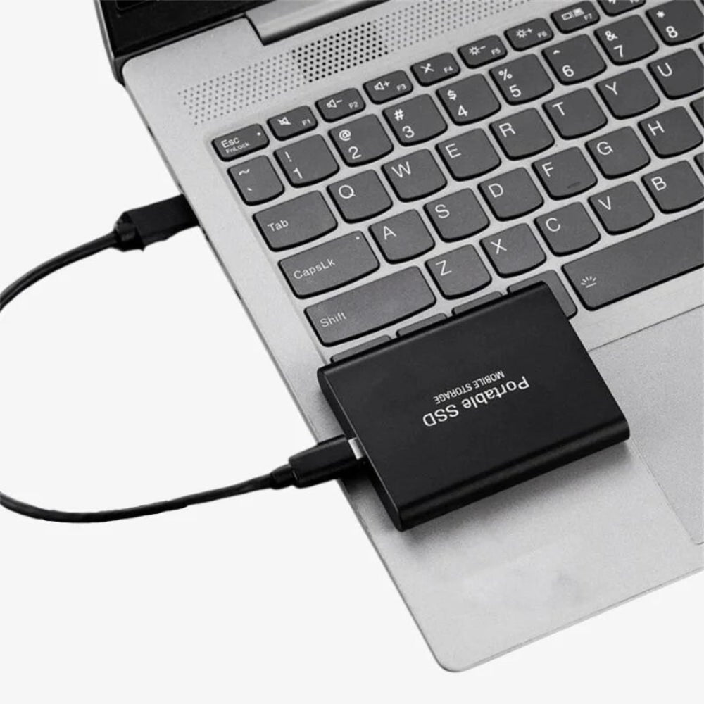 Portable external SSD connected to a laptop keyboard via USB cable