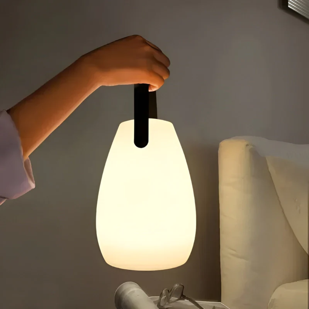 Portable waterproof wireless table lamp being carried by its handle next to a bed