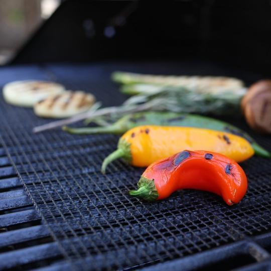 Fresh colorful bell peppers and vegetables roasting on a non-stick barbecue grill mat