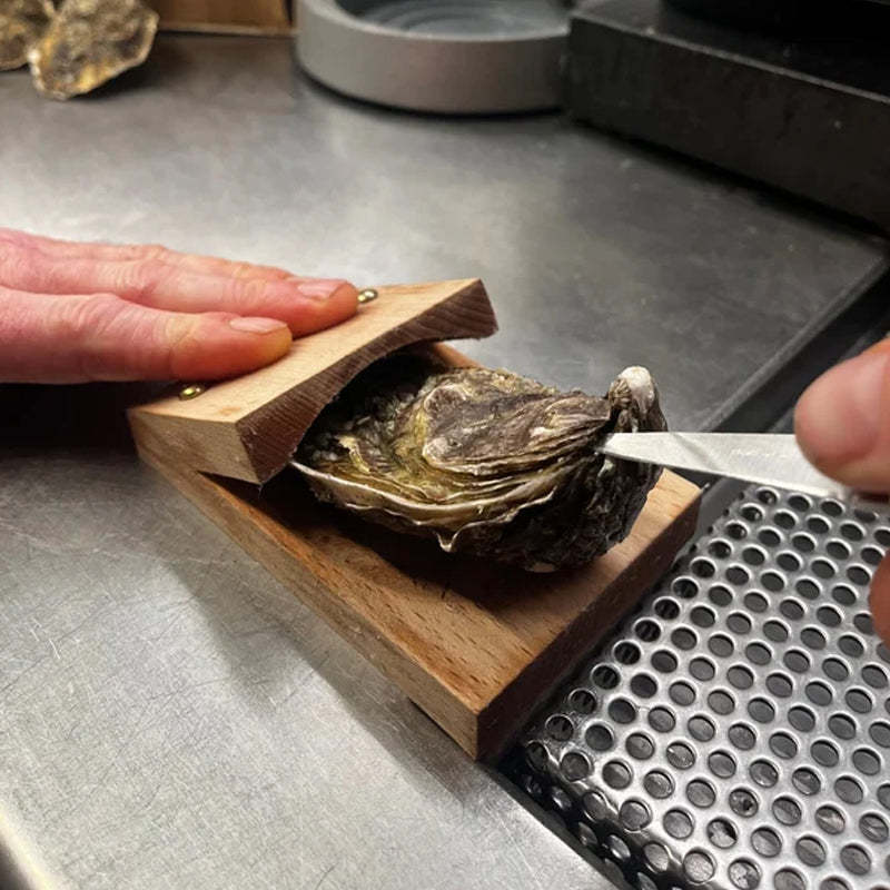Close-up of a wooden oyster shell opener clamp holding an oyster on a counter