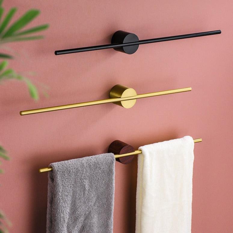 Three modern metal towel bars in various finishes mounted on a pink wall