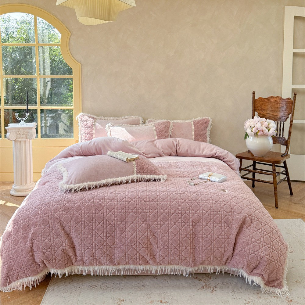 Pink quilted bedding set with fringe accents and matching decorative pillows on a made bed