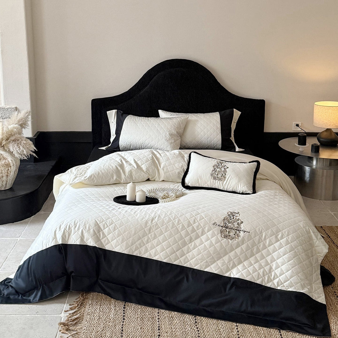 Quilted bedding set featuring floral embroidery and black and white contrast edge on a made bed
