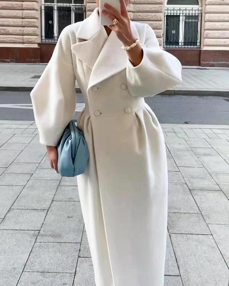 Woman wearing a white double-breasted long coat with oversized sleeves on a city street