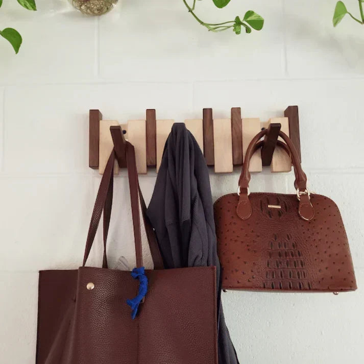 Wooden piano coat rack featuring two-tone walnut and beech blocks with brown leather bags hanging on deployed hooks