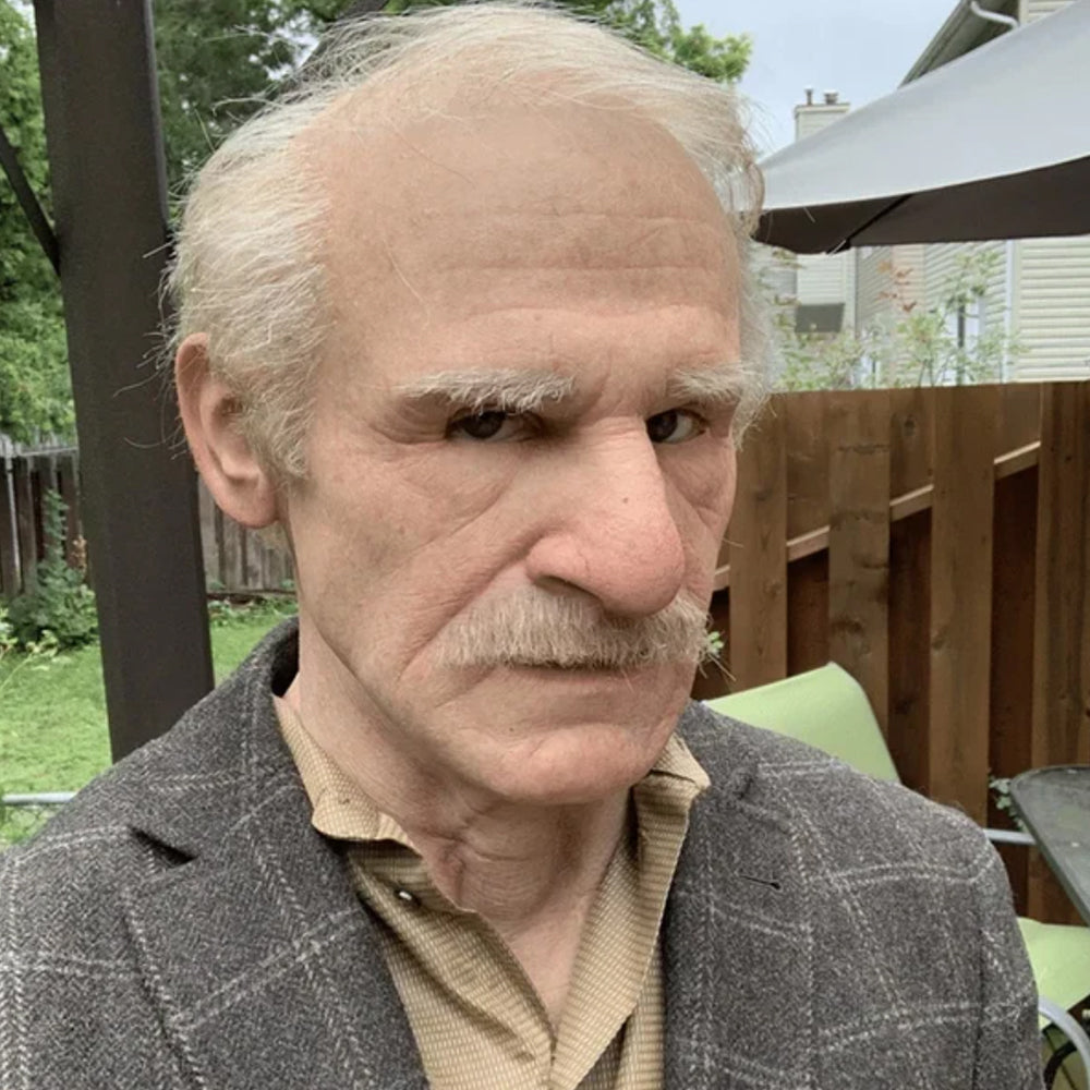 Close-up portrait of a realistic old man mask with detailed wrinkles and gray hair in an outdoor setting