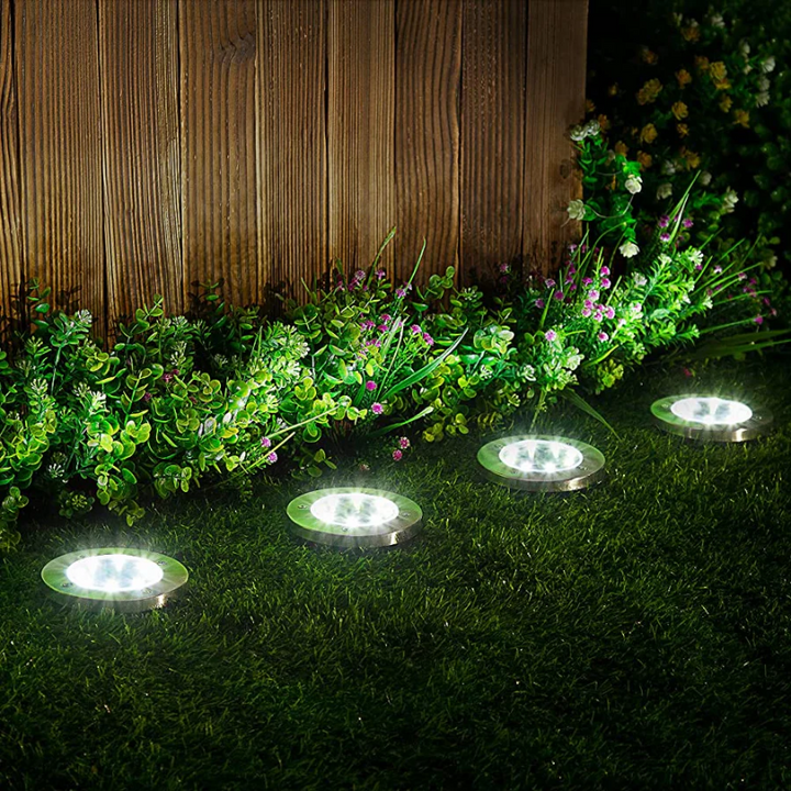 Close-up of circular solar ground lights glowing along a garden flower bed