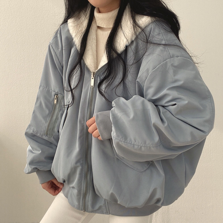 Front view of a woman wearing a light blue winter jacket with a hood and zipper pockets