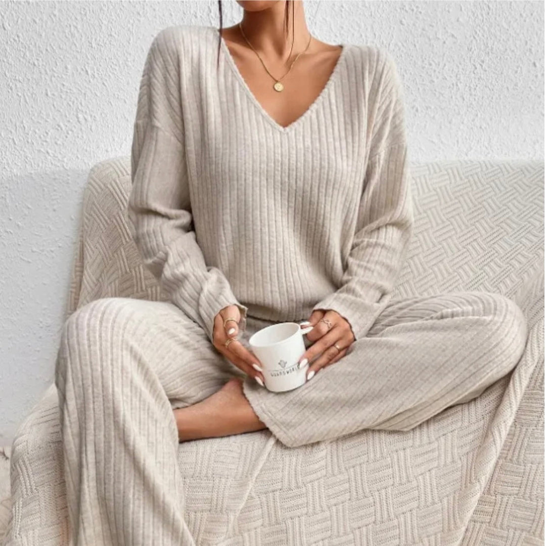 Woman sitting on a couch wearing a beige knit loungewear set with a V-neck top and holding a mug.