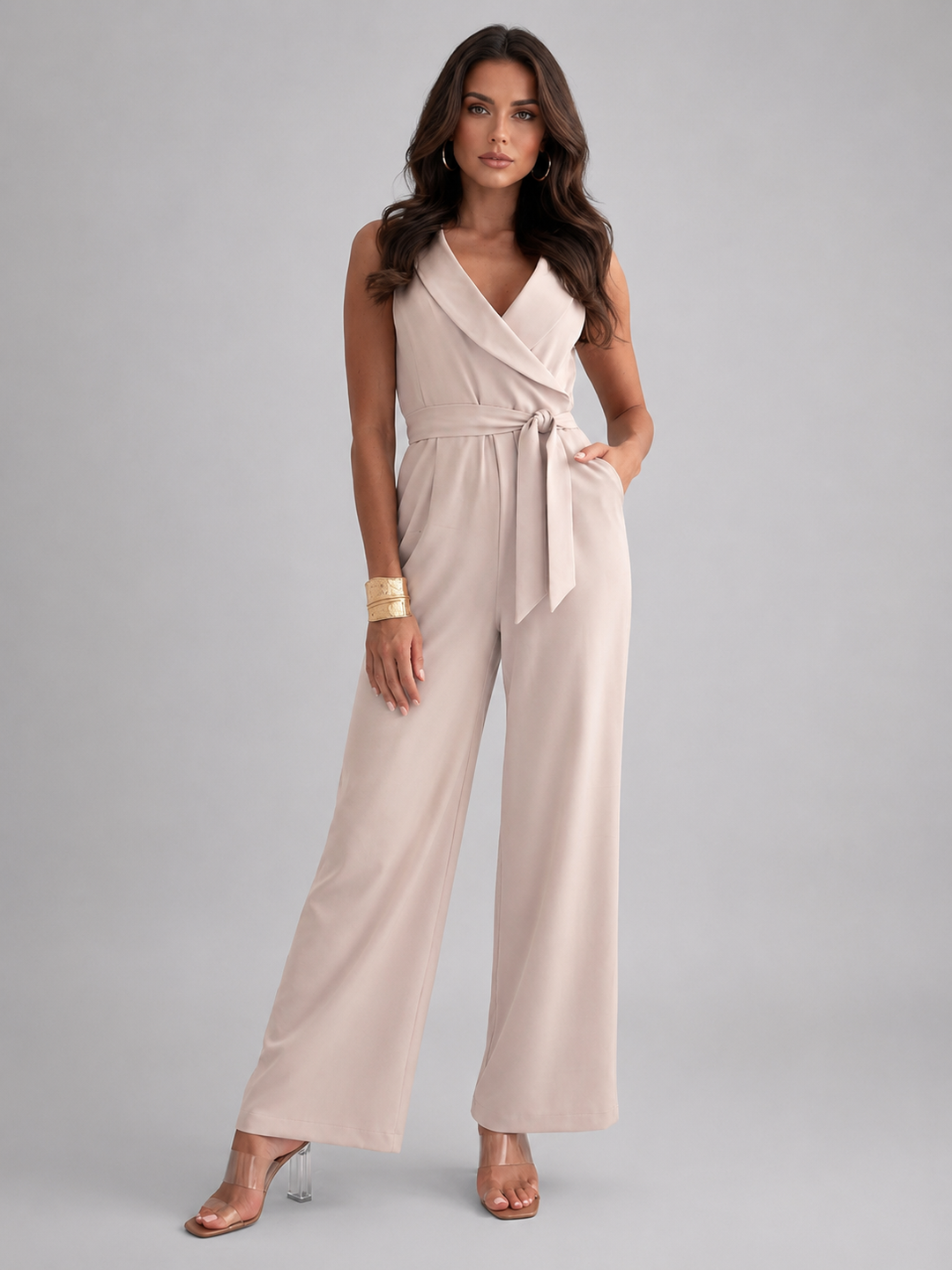 Front view of a woman wearing an elegant sleeveless wide leg jumpsuit with a wrap V-neck and tie waist.