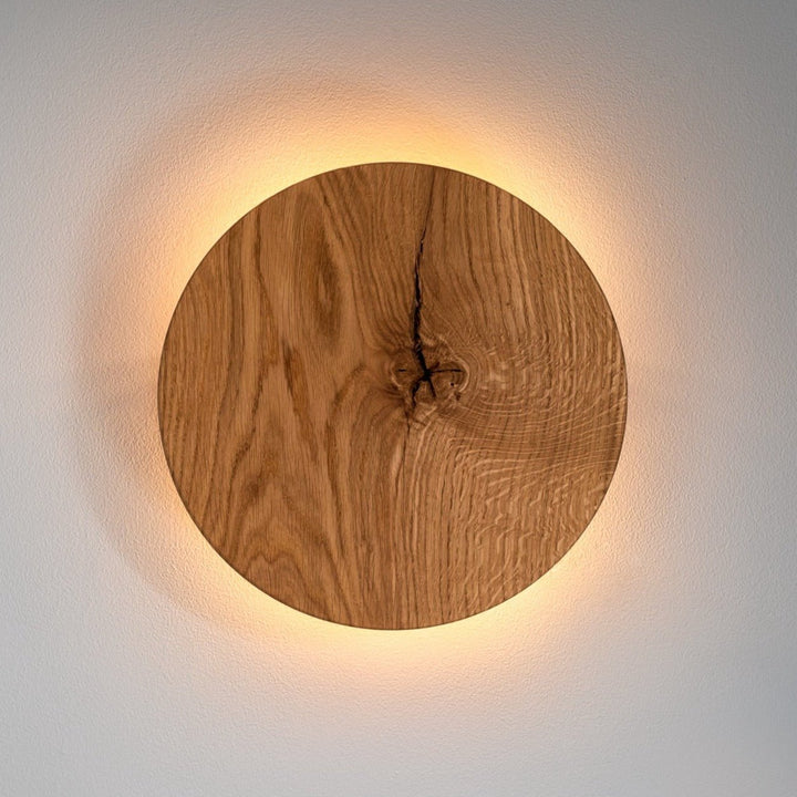 Close-up of the round wooden wall sconce showing the warm halo glow against a light wall.