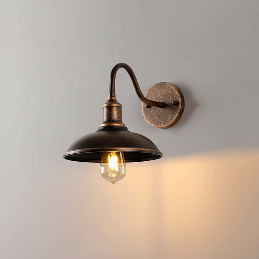 Rustic outdoor wall lamp in antique brass with warm LED bulb glowing against a neutral wall