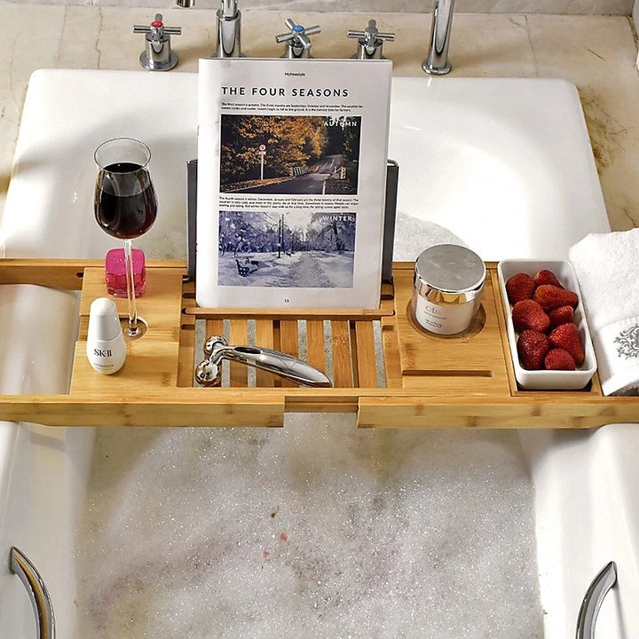 Close-up view of bamboo bath tray displaying a magazine, wine glass, and skincare products