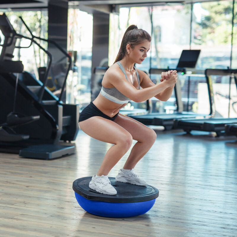 Woman exercising on a blue balance ball trainer in a gym