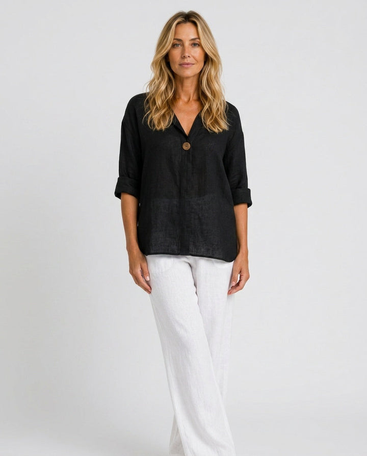 Front view of a woman wearing a black open collar top with white trousers