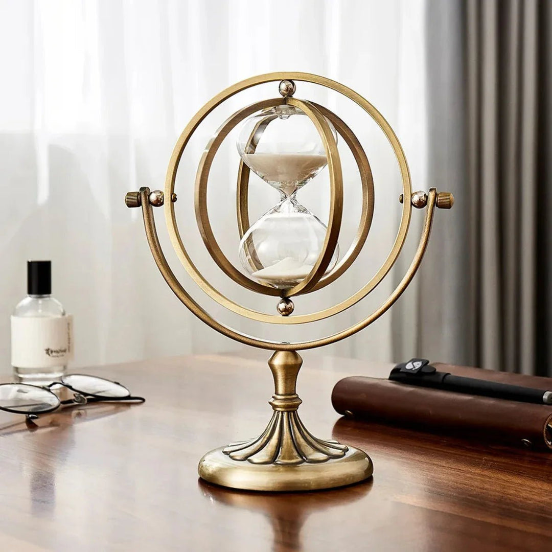 Minimalist metal sand hourglass timer displayed on a wooden desk next to a perfume bottle and notebook